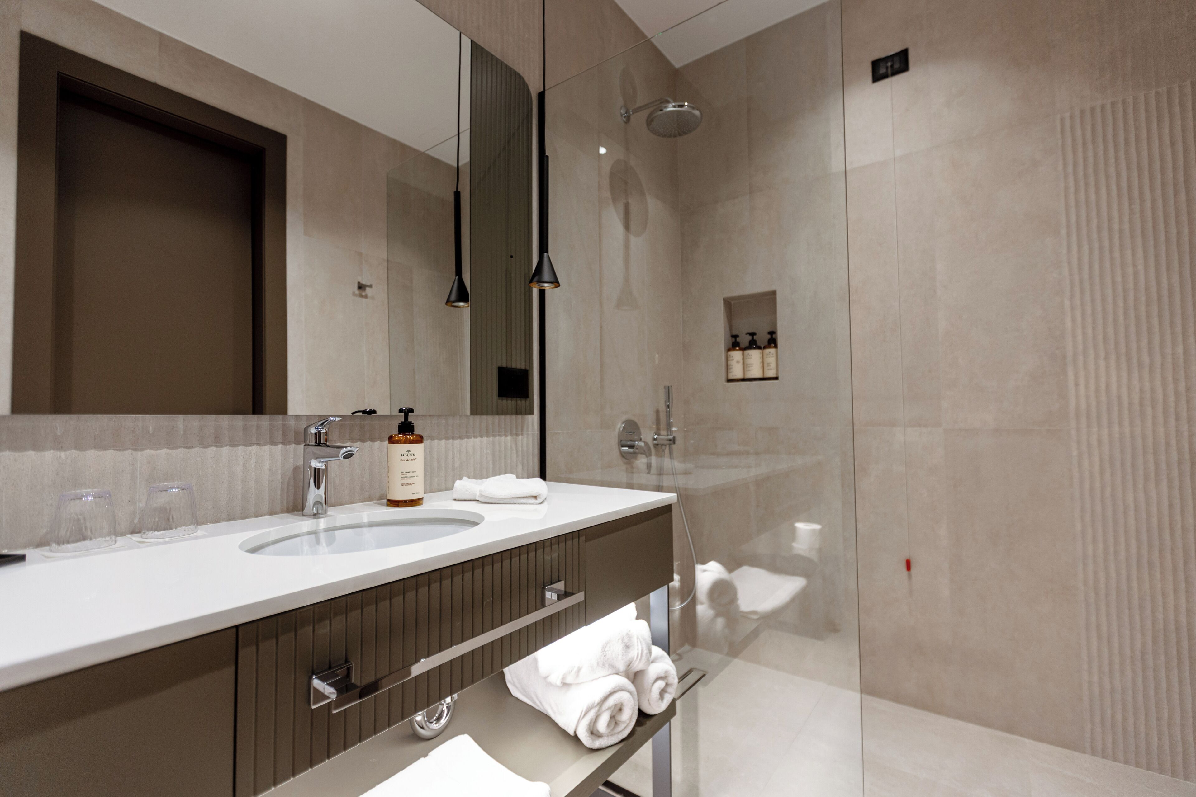 A modern bathroom with a large mirror, two sinks, a shower, and a towel rack.