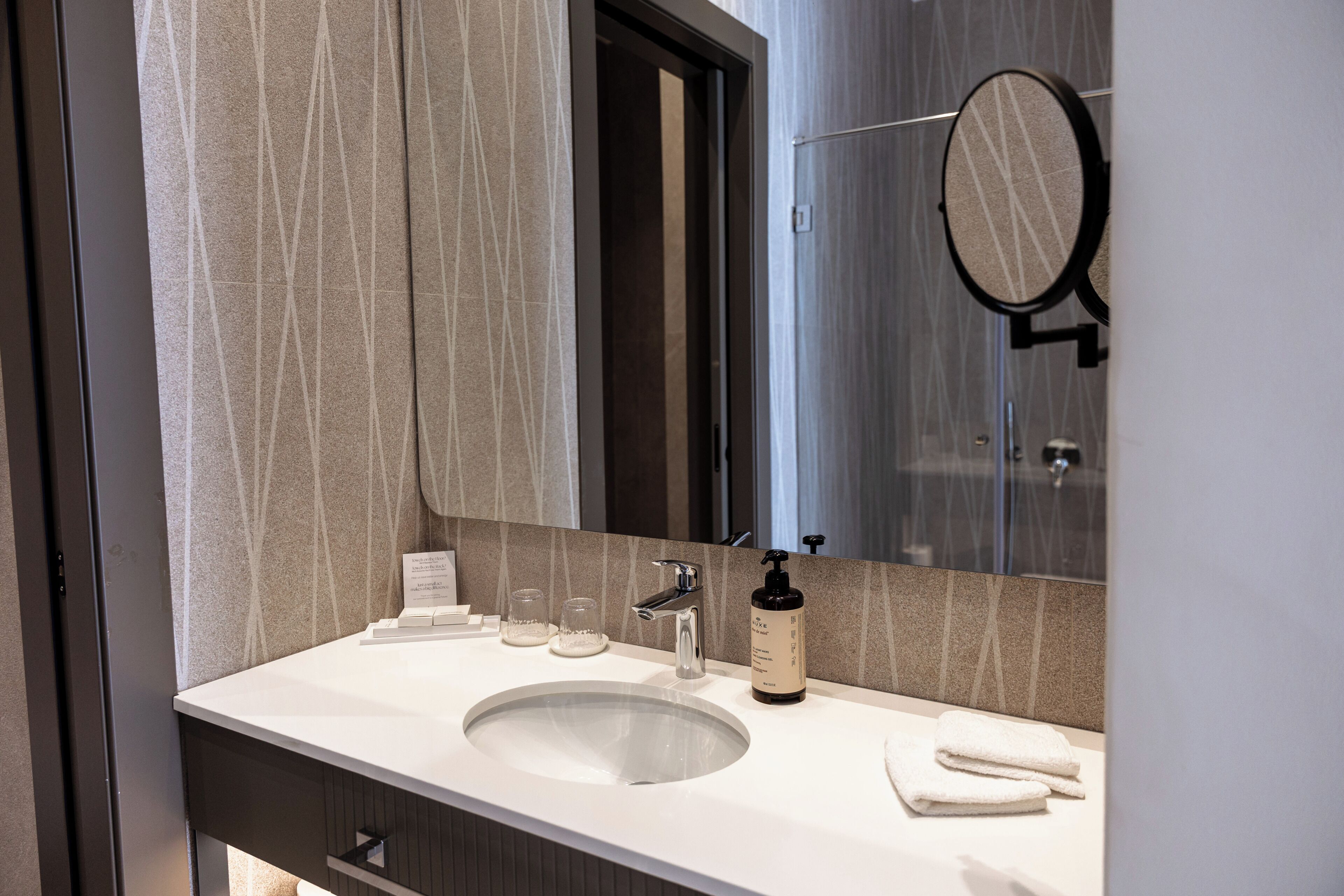 A bathroom with a white sink, a mirror, a towel, and a bottle of soap.