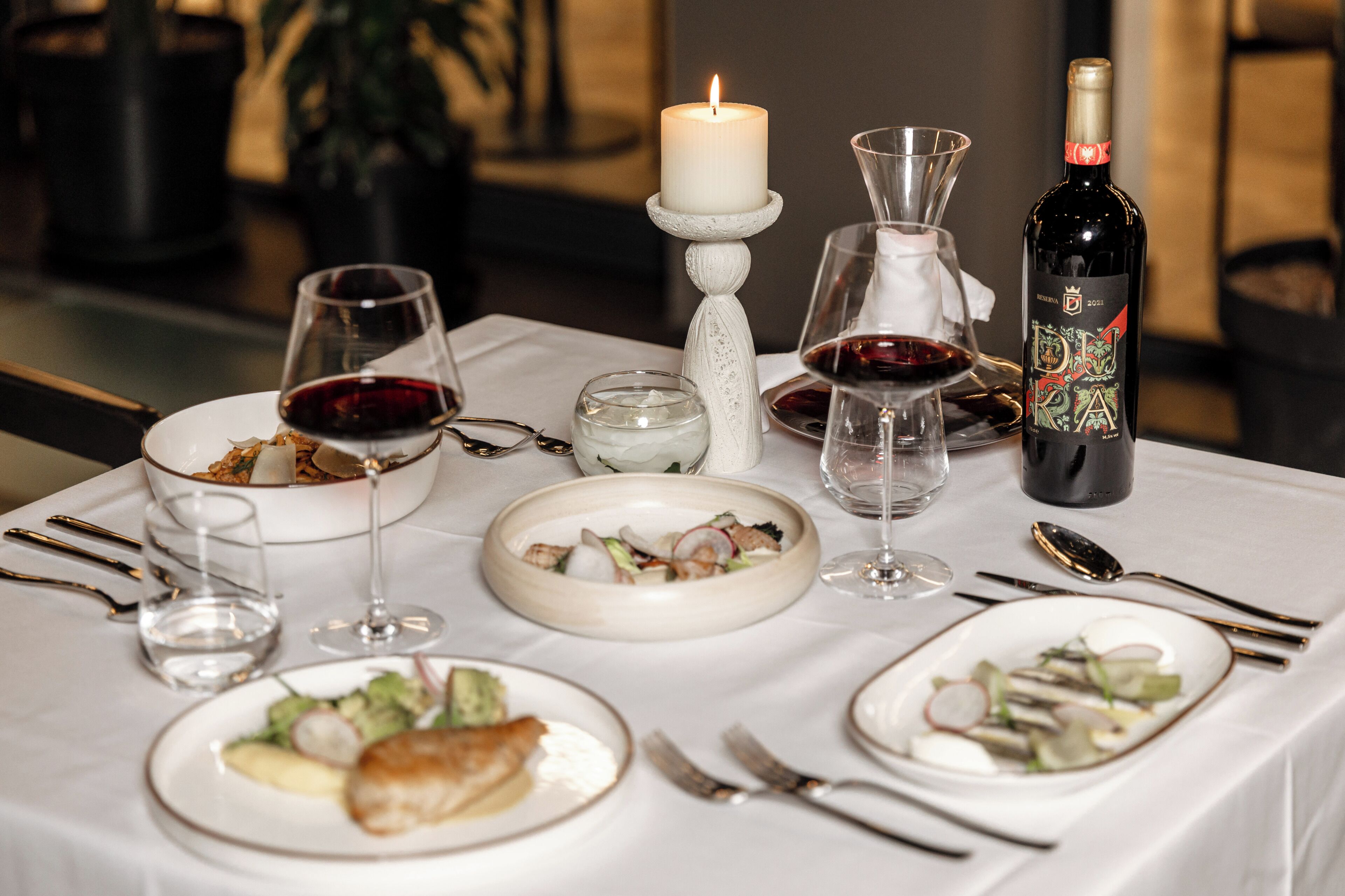 A dining table set with plates, glasses, a candle, and a bottle of wine.