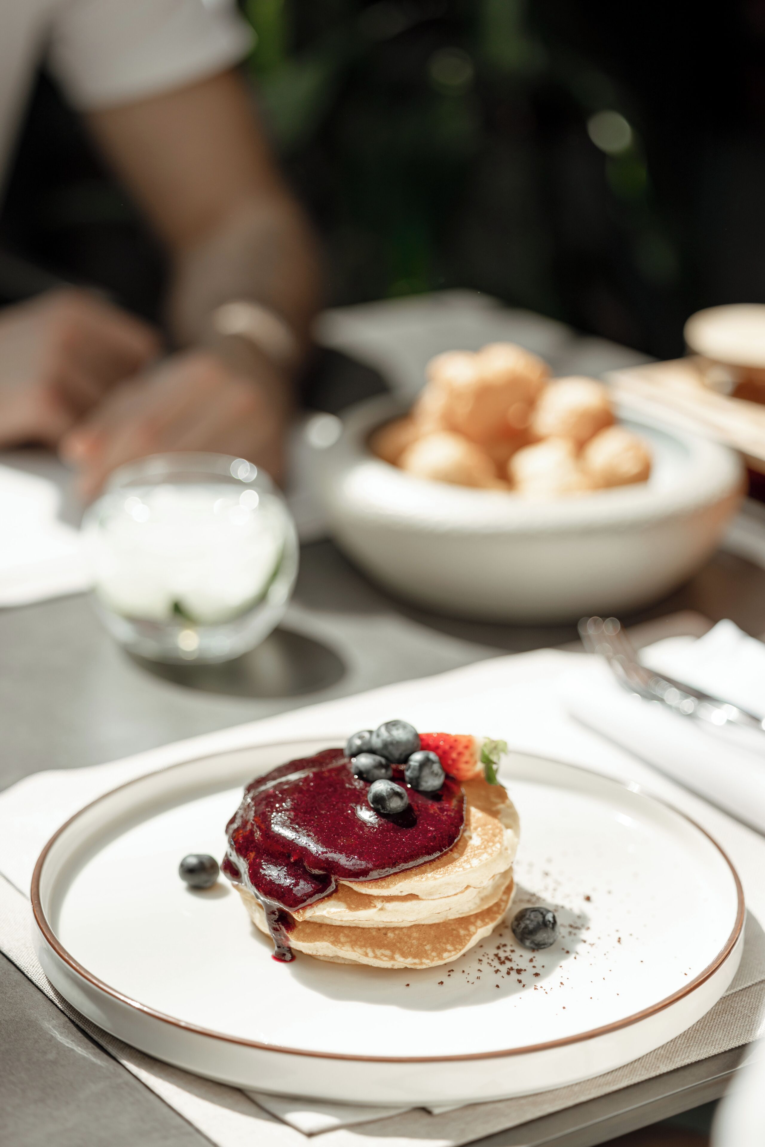 Ein Dessertteller mit Pfannkuchen, belegt mit Beeren, und im Hintergrund eine kleine Schüssel Croissants.