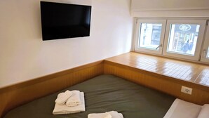 A hotel room with a bed, a flat-screen TV mounted on the wall, and a window with a view of the street. - CASA MORETTI (Bari)