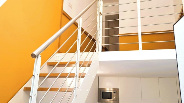 A modern staircase with white railings and wooden steps, leading to a lower level with a microwave and cabinets. - CASA MORETTI (Bari)