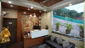 A reception area with a Buddha statue, a receptionist desk, a sofa, and a view of a green landscape. - Royal suites Chakki Morh (Kasauli)