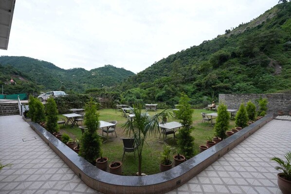 A terrace with outdoor seating, surrounded by potted plants and overlooking a mountainous landscape. - Royal suites Chakki Morh (Kasauli)