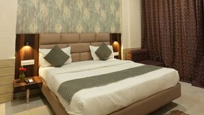 A bedroom with a large bed, a ceiling fan, a nightstand with a lamp, and a window with curtains. - Royal suites Chakki Morh (Kasauli)