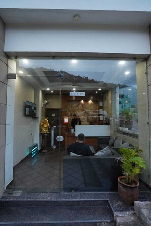 A reception area with a reception desk, a receptionist, and a receptionist's desk. There is a statue on the left and a potted plant on the right. - Royal suites Chakki Morh (Kasauli)