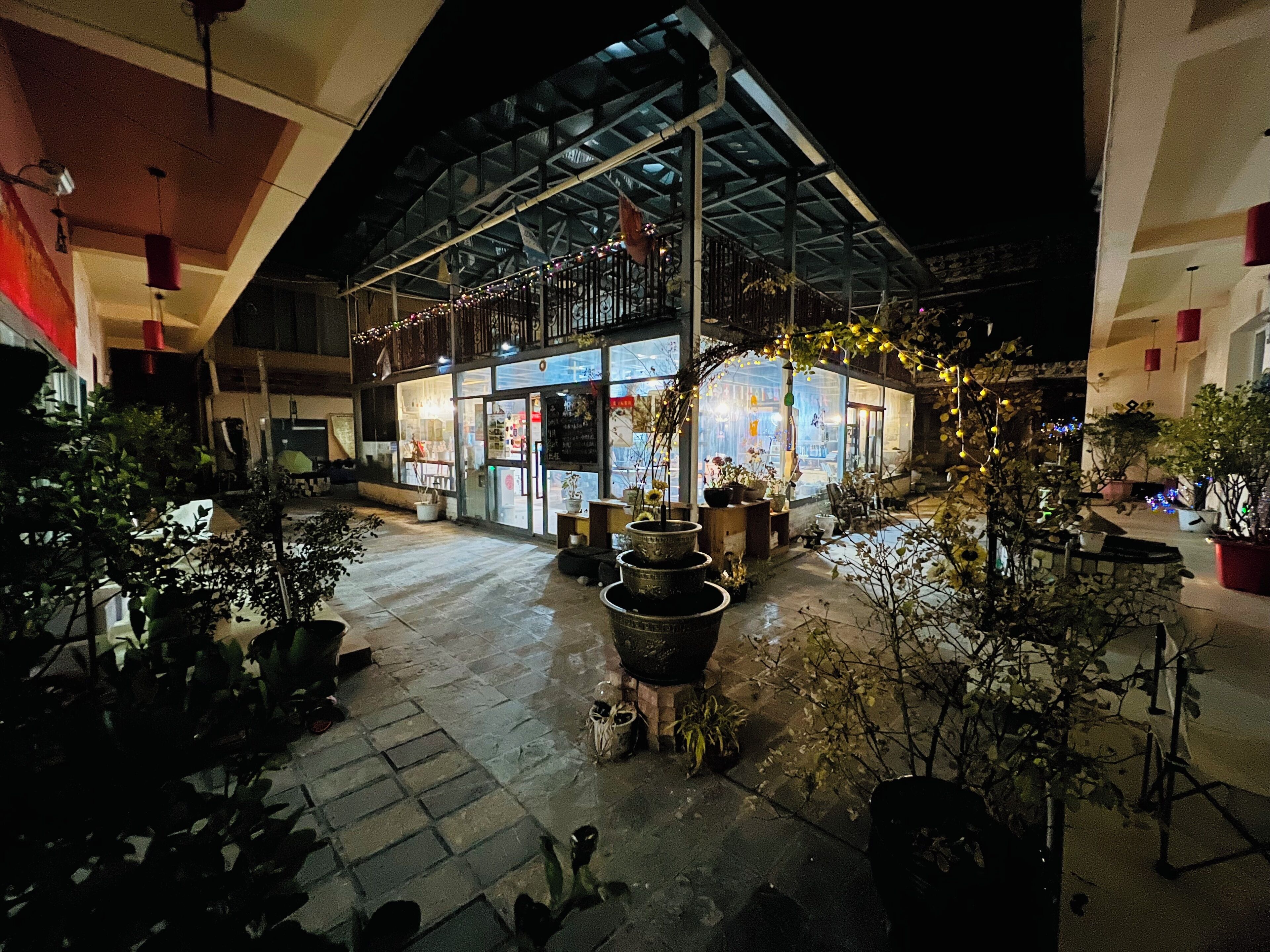 An outdoor courtyard with potted plants, a covered seating area, and a building with large windows.