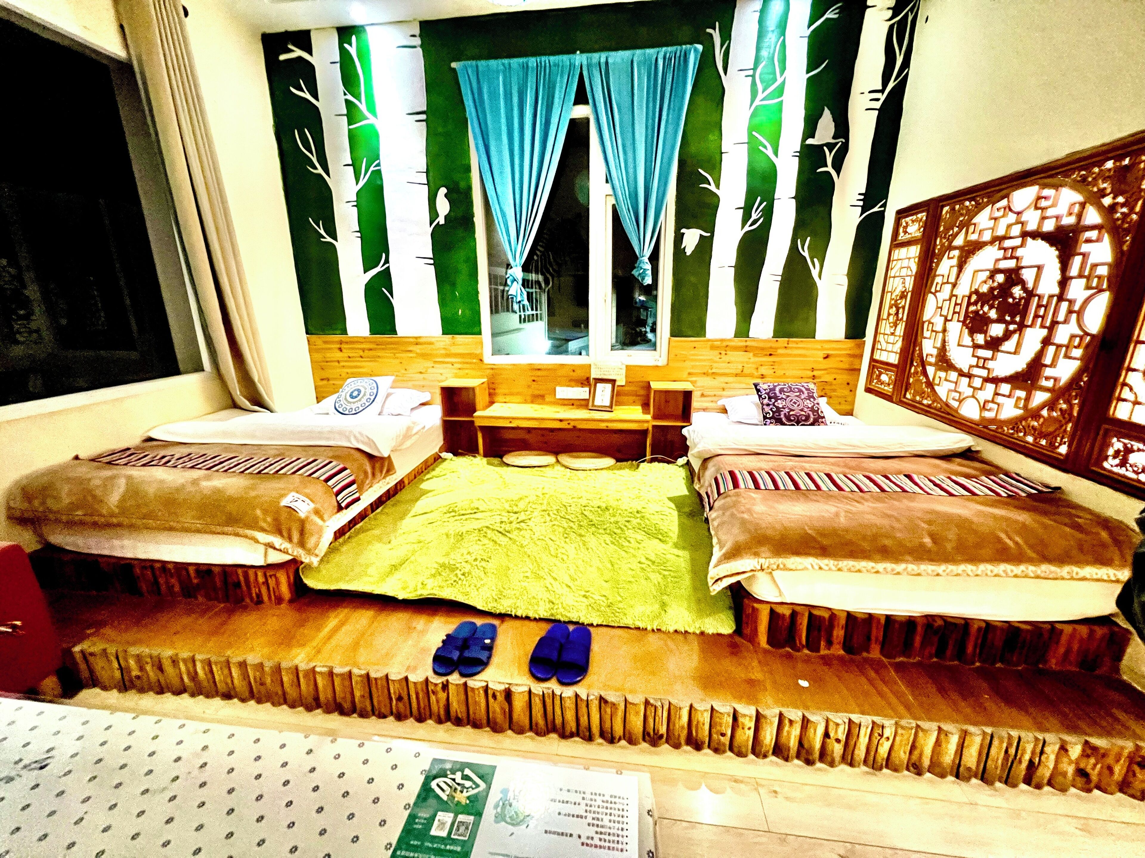 A room with two beds, a window with blue curtains, a wooden headboard, and a decorative wall panel.