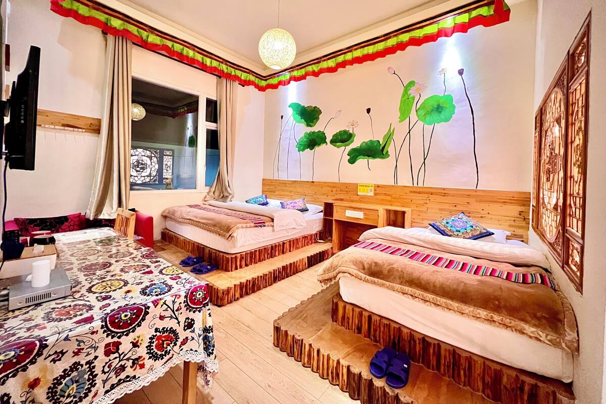Een kamer met twee bedden, een tafel met een tafelkleed met patroon, en een muur met een bloemenmural.