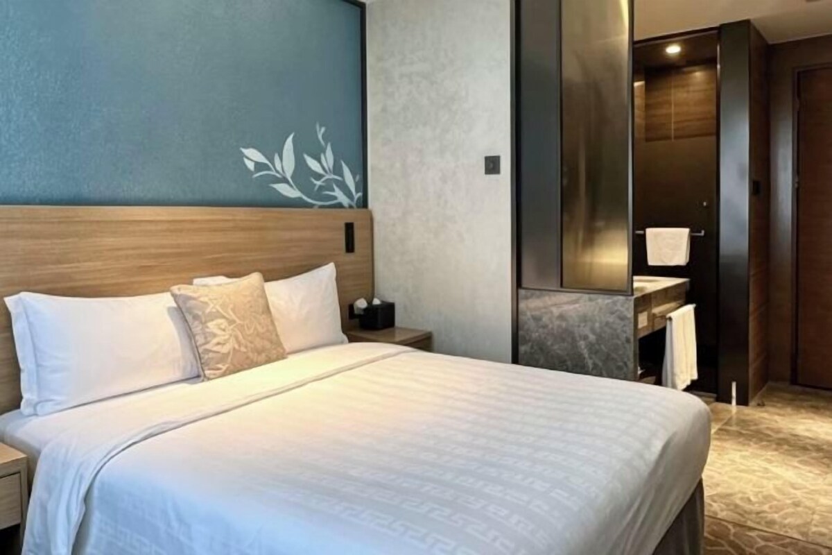 A hotel room with a bed, a nightstand, a bathroom with a mirror, and a towel rack.