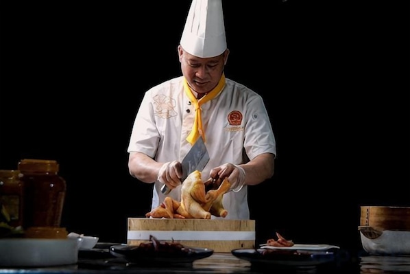 Un chef con uniforme blanco y gorro de chef preparando comida sobre una tabla de madera.