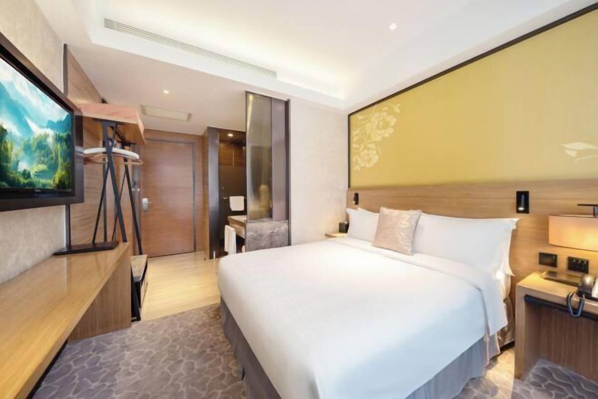Habitación de hotel moderna con una cama grande, un televisor sobre un mueble de madera, un espejo y una pared con diseño floral.