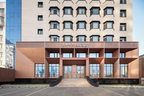 Un hotel con fachada moderna, varios pisos y una entrada central con rampa de acceso a las puertas.