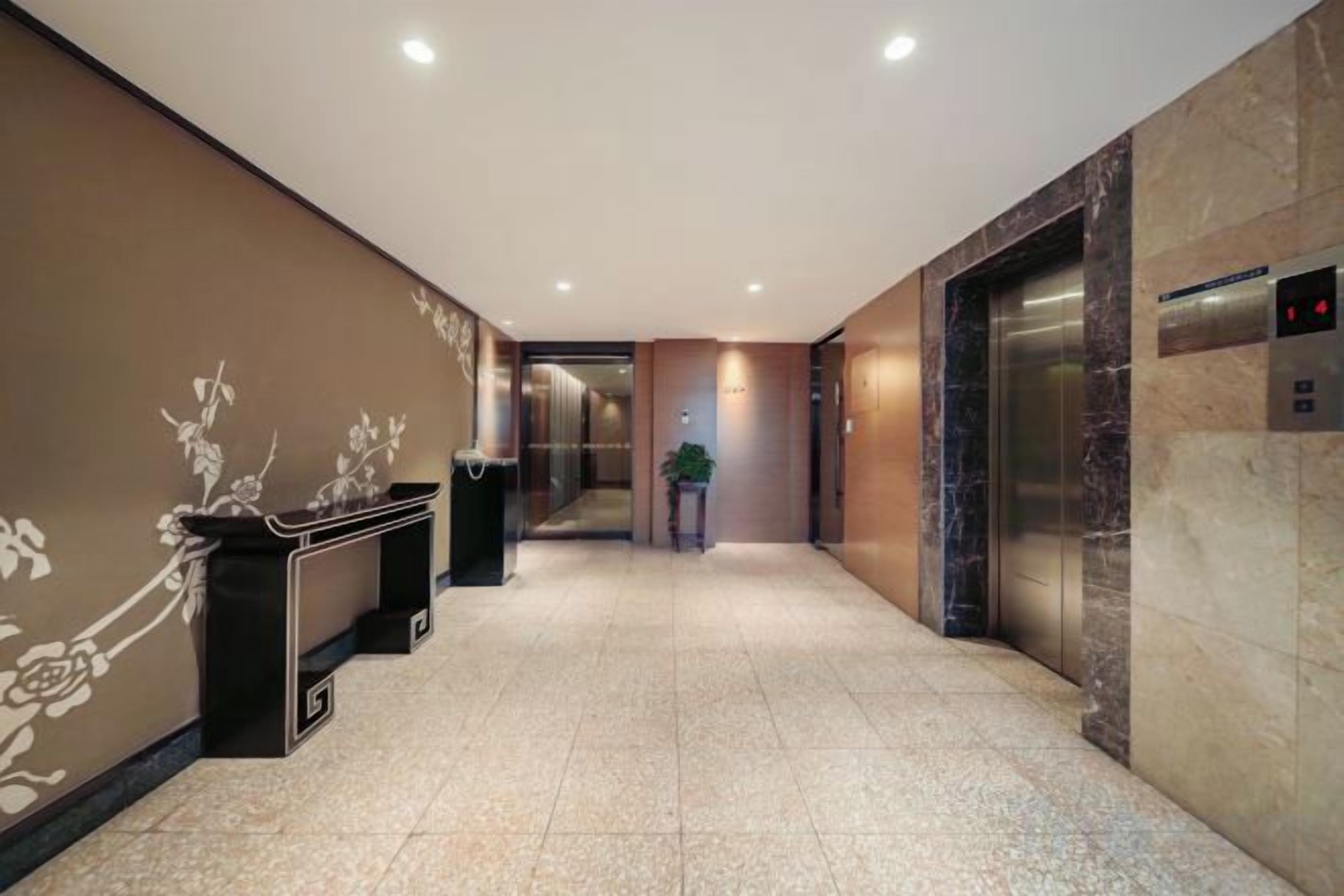A hotel lobby with a reception desk, a trash bin, an elevator, and a potted plant.