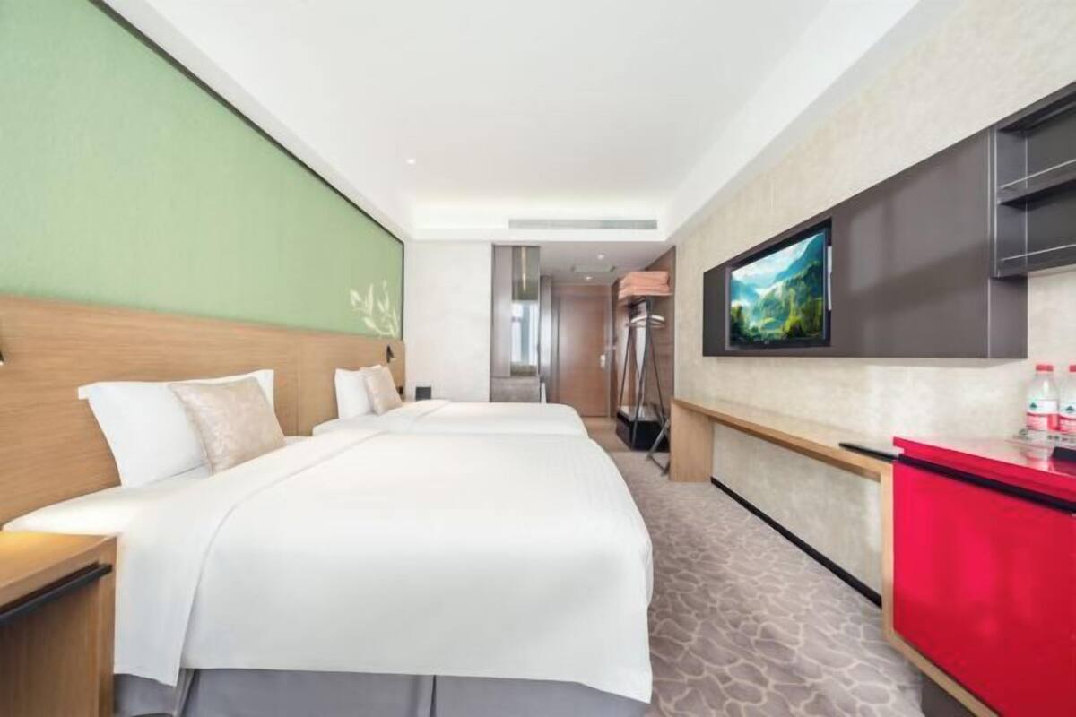 Una habitación de hotel con una cama grande, un televisor montado en la pared y un minibar rojo.