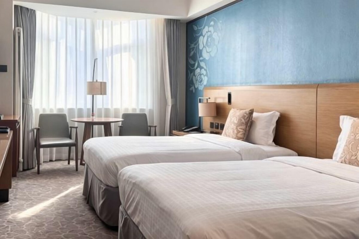 Une chambre d’hôtel avec deux lits, un bureau, une chaise et une fenêtre avec des rideaux.