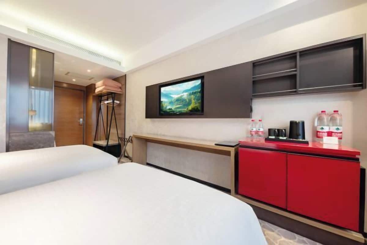 Una habitación de hotel con una cama, un televisor en la pared, un minibar rojo y un escritorio de madera.