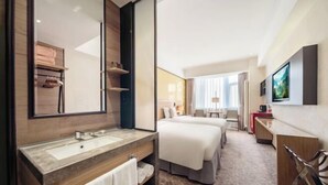 A hotel room with a large mirror, a sink, two beds, a desk, and a TV.