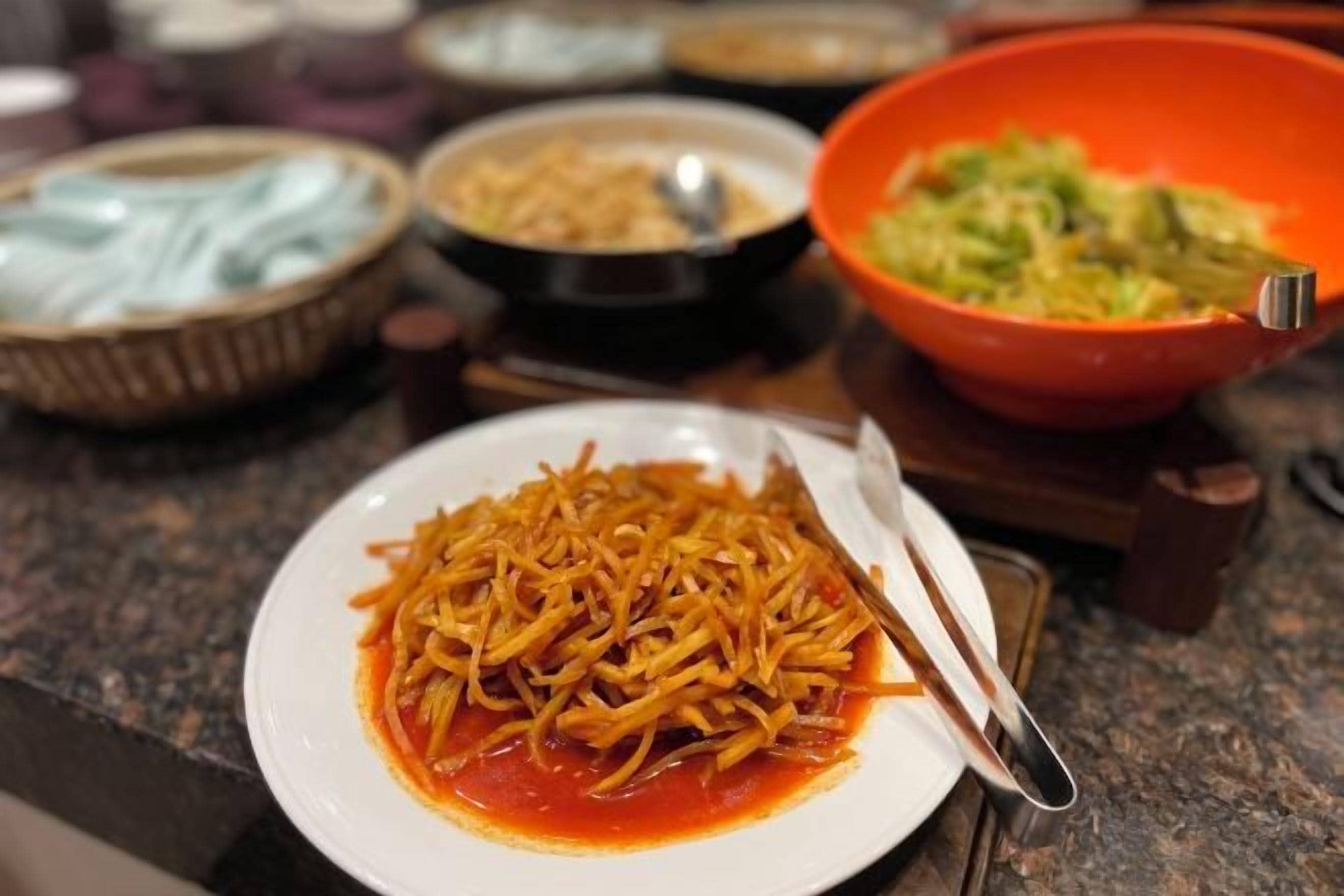 Una mesa de comedor con diferentes platos, entre ellos un plato de fideos y un bol de verduras.