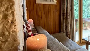 A cozy room with a wooden ceiling, a framed picture on the wall, a candle on a table, and a view of greenery outside. - Residences Delavay (Les Gets)