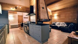 A modern kitchen with a central island, a dining area with a wooden table, and a cozy seating area with a sofa and a blanket. - Residences Delavay (Les Gets)
