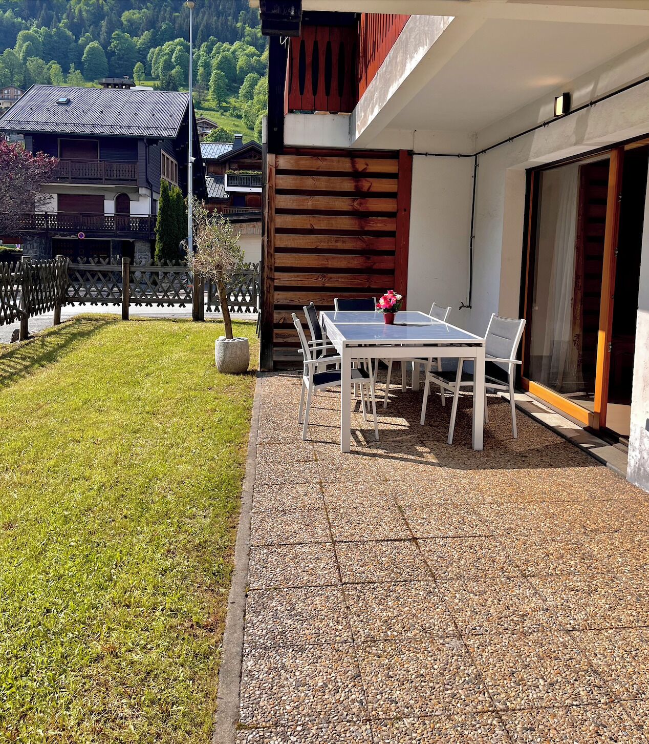 A patio with a table and chairs, a small garden, and a view of a mountain.