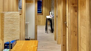 A wooden interior with a central hallway leading to a room with a table and chair. - Residences Delavay (Les Gets)
