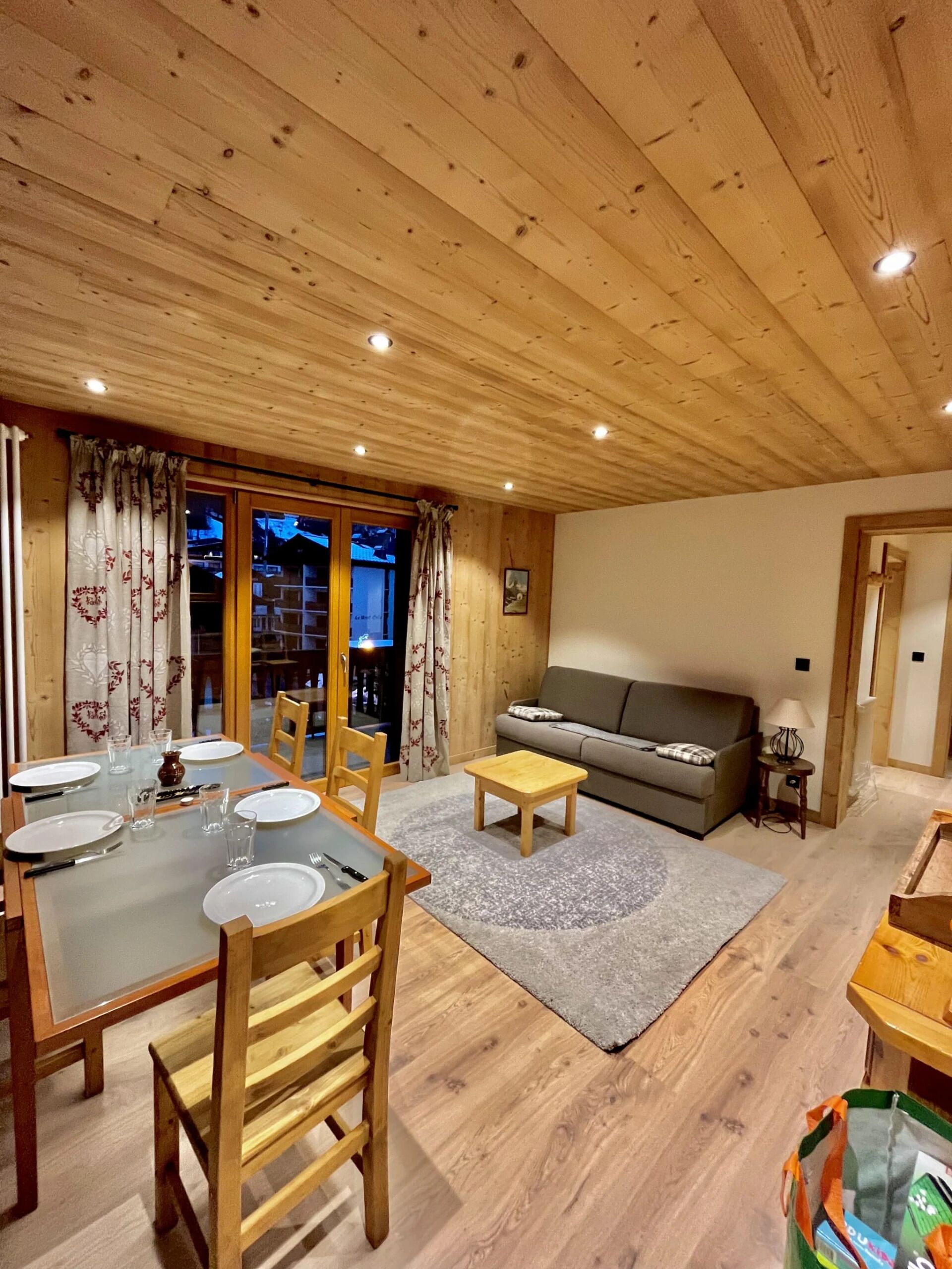 Une salle à manger aux murs lambrés, avec une table dressée pour quatre personnes, un canapé et une petite table d’appoint.