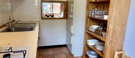 A kitchen with a stove, sink, and wooden cabinets. There is a window with a view of houses outside.