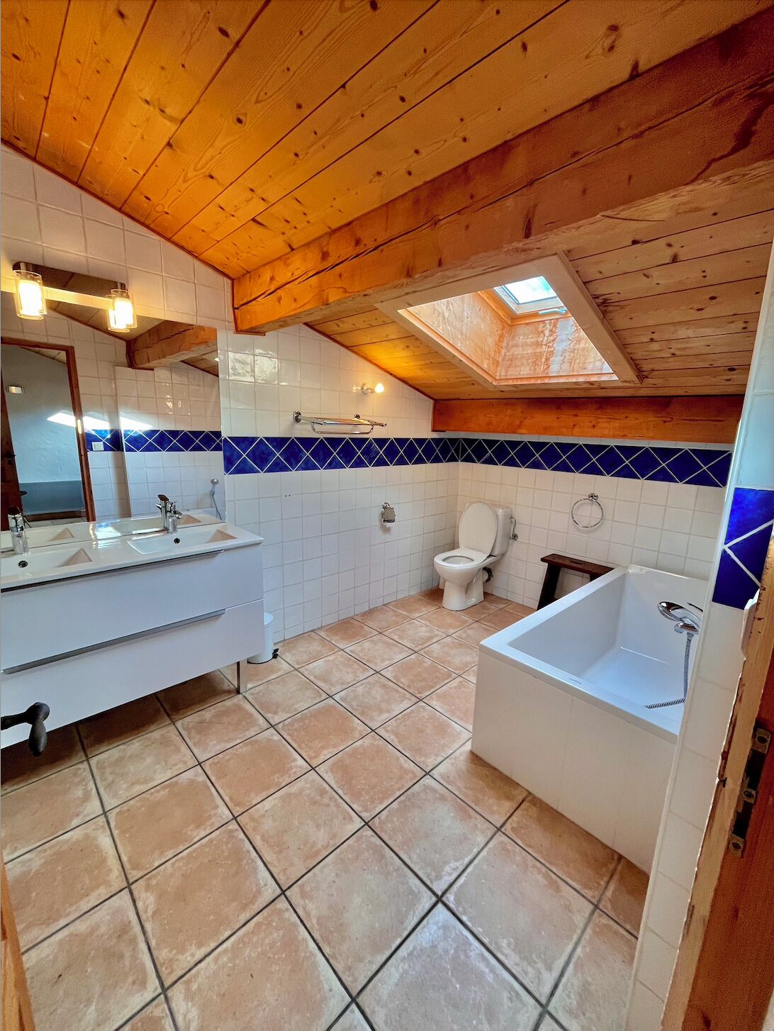 Un baño con techo de madera, tragaluz, lavamanos blanco, inodoro y bañera.