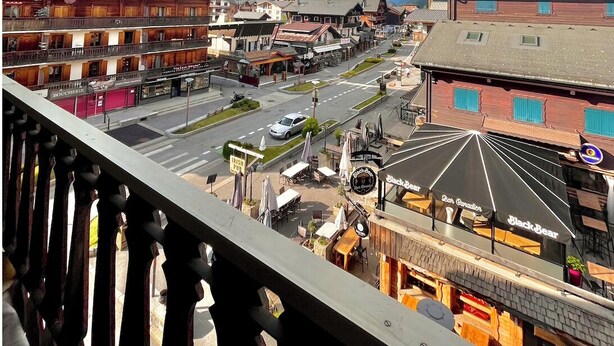A town with a main street, buildings, and a mountain in the background. - Residences Delavay (Les Gets)