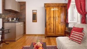 A compact living space with a kitchenette, a wooden wardrobe, a sofa with a patterned cushion, and a fruit bowl on the floor. - Sun Spalato Ammarulla (Split)