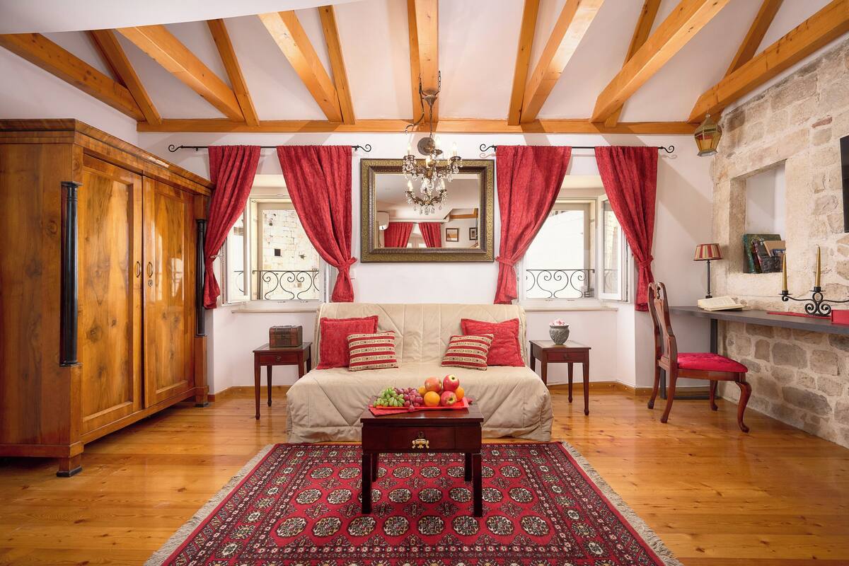 Ein Schlafzimmer mit einem Holzschrank, einem Bett mit roten Vorhängen, einer Chandelier und einer Steinwand.