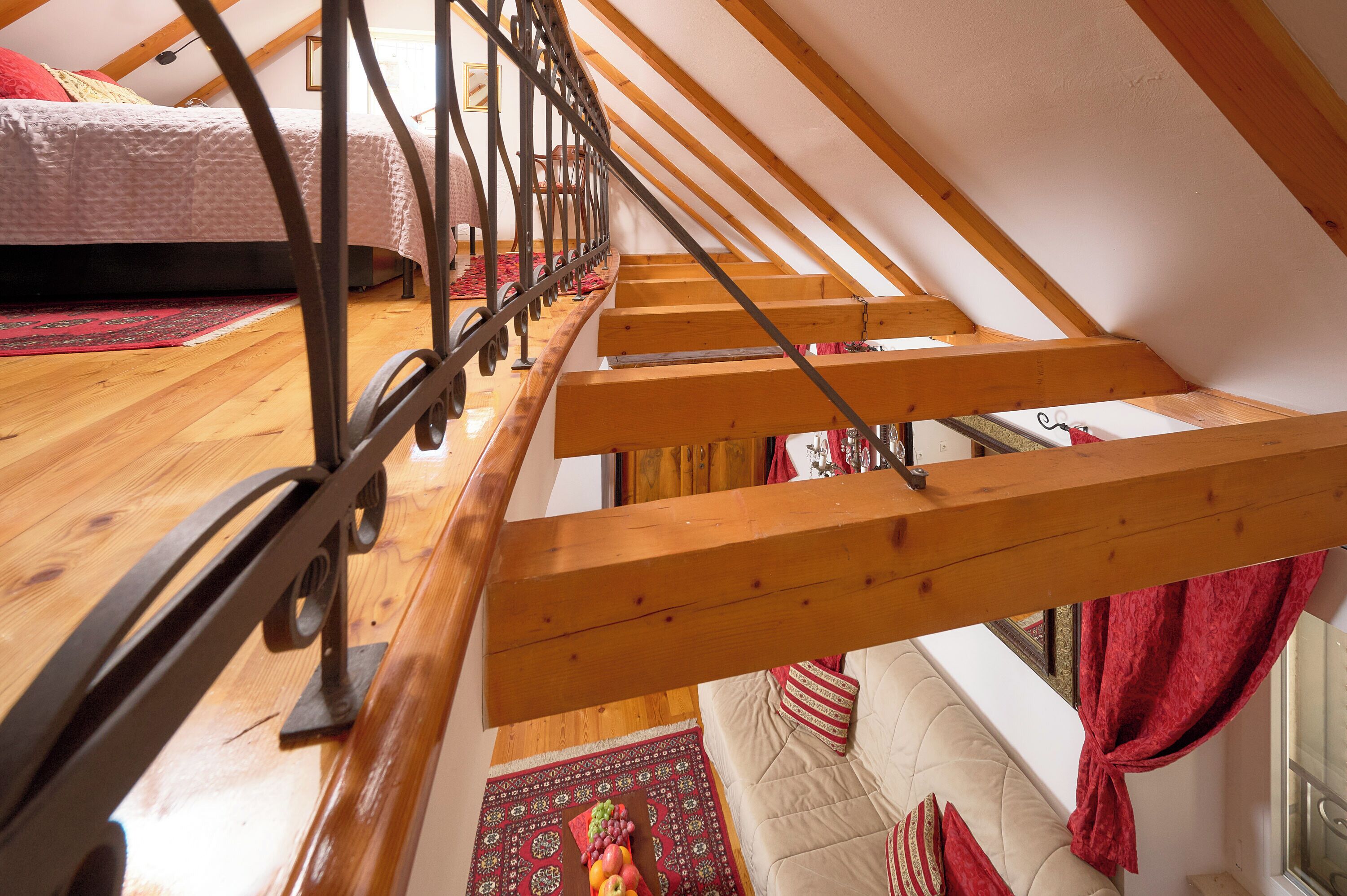 Une chambre à coucher aménagée dans un espace ouvert, avec un escalier en bois, un lit, un canapé et une fenêtre ornée de rideaux rouges.