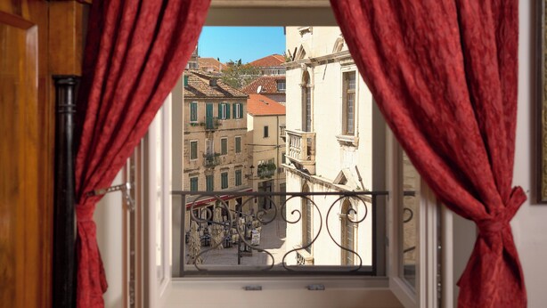 A balcony with red curtains, overlooking a street with buildings and a mountain in the background. - Sun Spalato Ammarulla (Split)