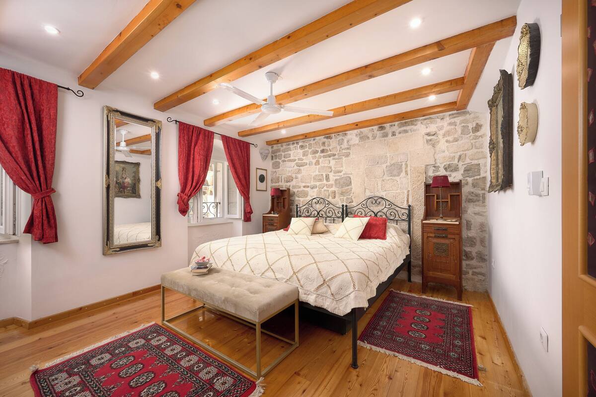 Ein Schlafzimmer mit einem Bett, Holzbalken, einer Steinwand, einem Spiegel und einem roten Teppich.