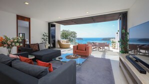 A modern living room with a sofa, armchairs, and a coffee table. There is a TV mounted on the wall and a view of the ocean through large windows. - Panoramic View The Heights Kata Beach B1 (Muang)