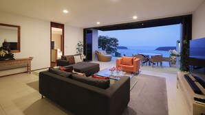 A modern living room with a sofa, coffee table, and a piano, featuring a large window with a view of the sea. - Panoramic View The Heights Kata Beach B1 (Muang)