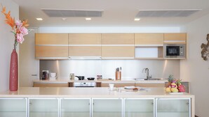 A modern kitchen with wooden cabinets, a microwave, and a central island with a fruit bowl. - Panoramic View The Heights Kata Beach B1 (Muang)