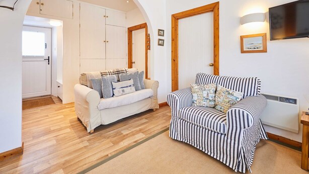 A living room with a white sofa and a striped armchair, wooden flooring, and a TV mounted on the wall. - Host Stay Spinnaker (Alnwick)