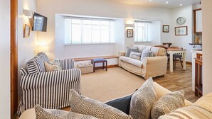 A cozy living room with striped and patterned sofas, a wooden bench, and a dining area with a table and chairs. - Host Stay Spinnaker (Alnwick)