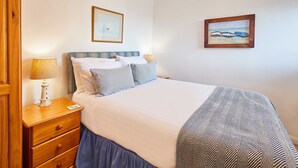 A neatly made bed with a striped headboard, a bedside table with a lamp, and two framed pictures on the wall. - Host Stay Spinnaker (Alnwick)