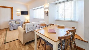 A cozy living room with a wooden dining table, striped sofa, and a TV mounted on the wall. - Host Stay Spinnaker (Alnwick)