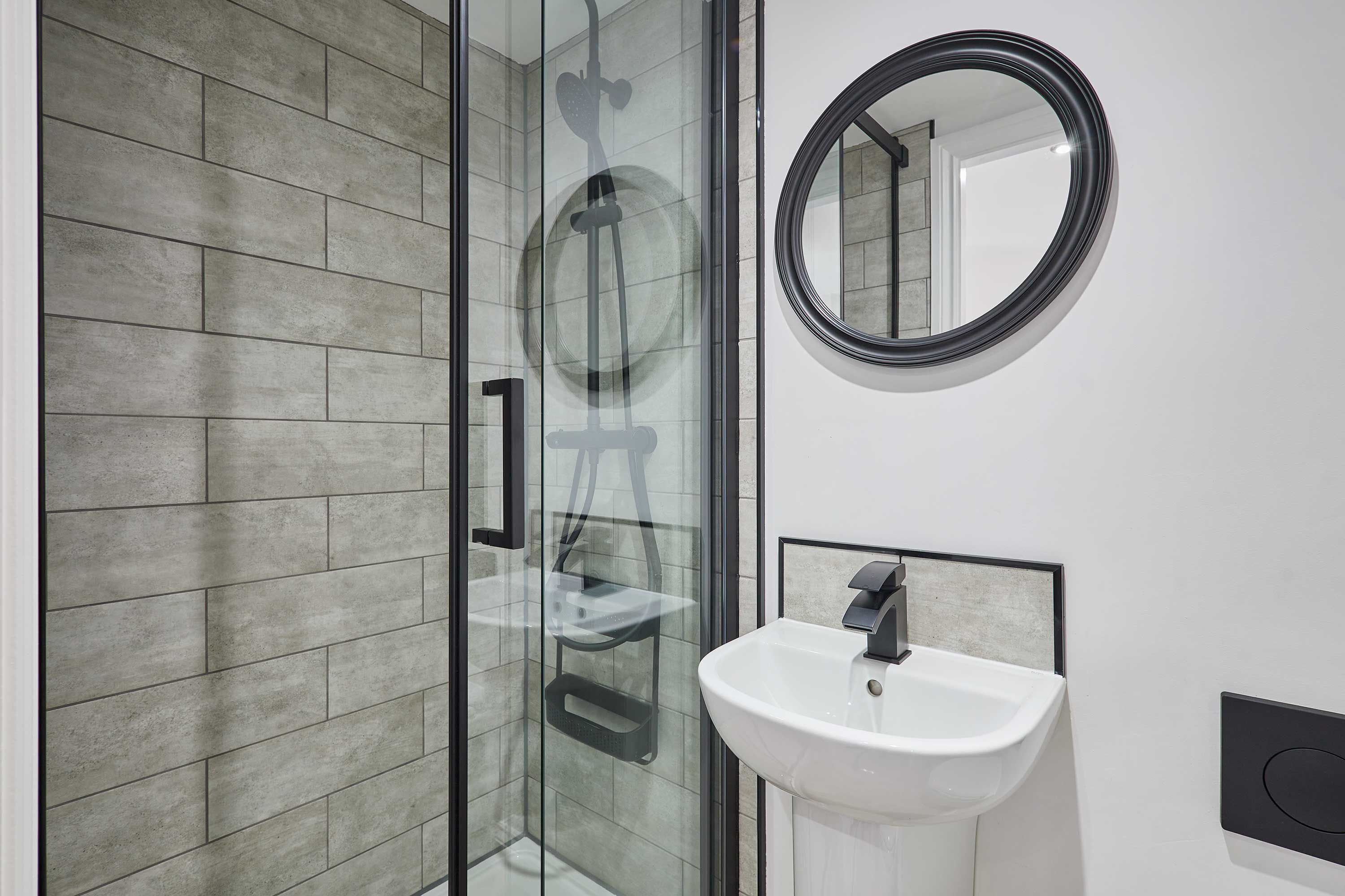 A modern bathroom with a glass shower enclosure, a white sink, and a round mirror.