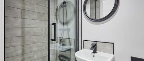 A modern bathroom with a glass shower enclosure, a white sink, and a round mirror.