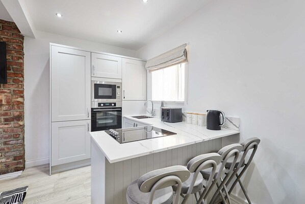 A modern kitchen with white cabinets, a built-in microwave, oven, and a large island with bar stools.