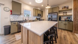 Una cocina moderna con una isla grande, armarios de madera, electrodomésticos de acero inoxidable e iluminación colgante.