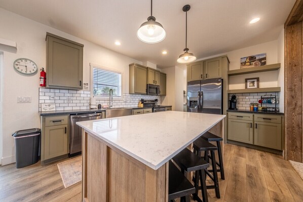 Una cocina moderna con una isla grande, armarios de madera, electrodomésticos de acero inoxidable e iluminación colgante.