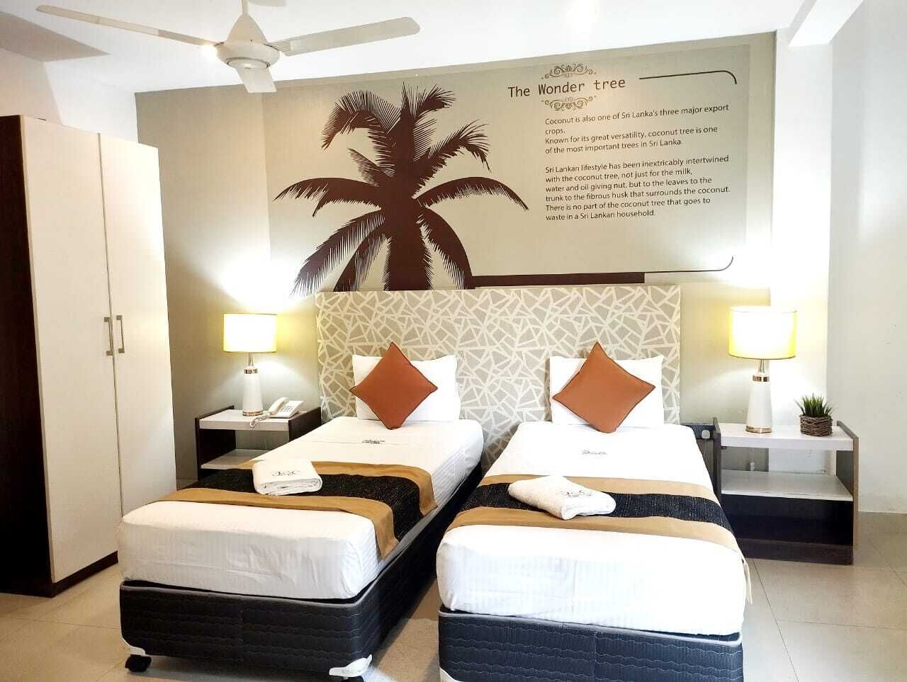 A hotel room with two single beds, a large palm tree mural, and a ceiling fan.