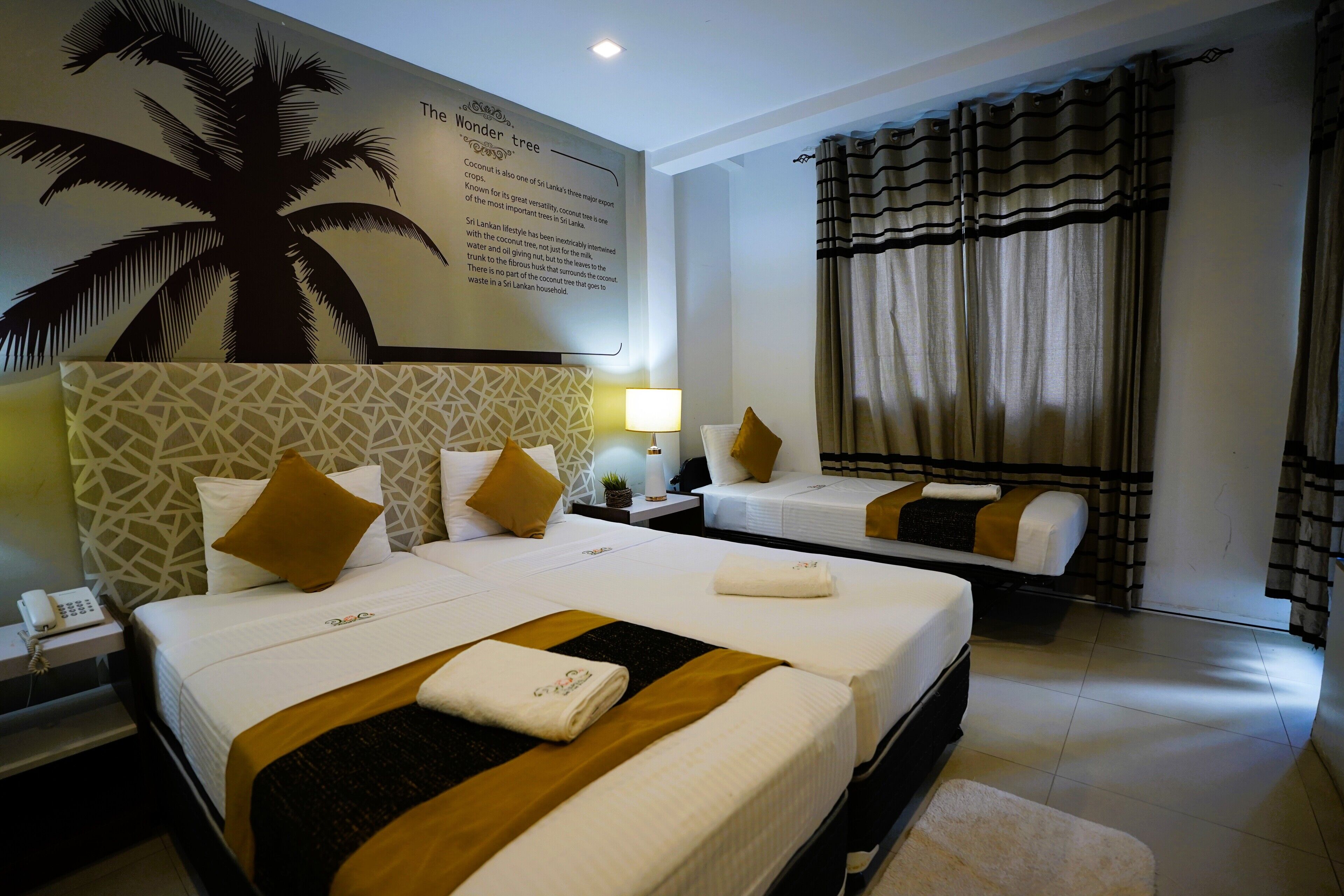 A hotel room with two beds, a patterned headboard, a large palm tree mural, and a window with curtains.